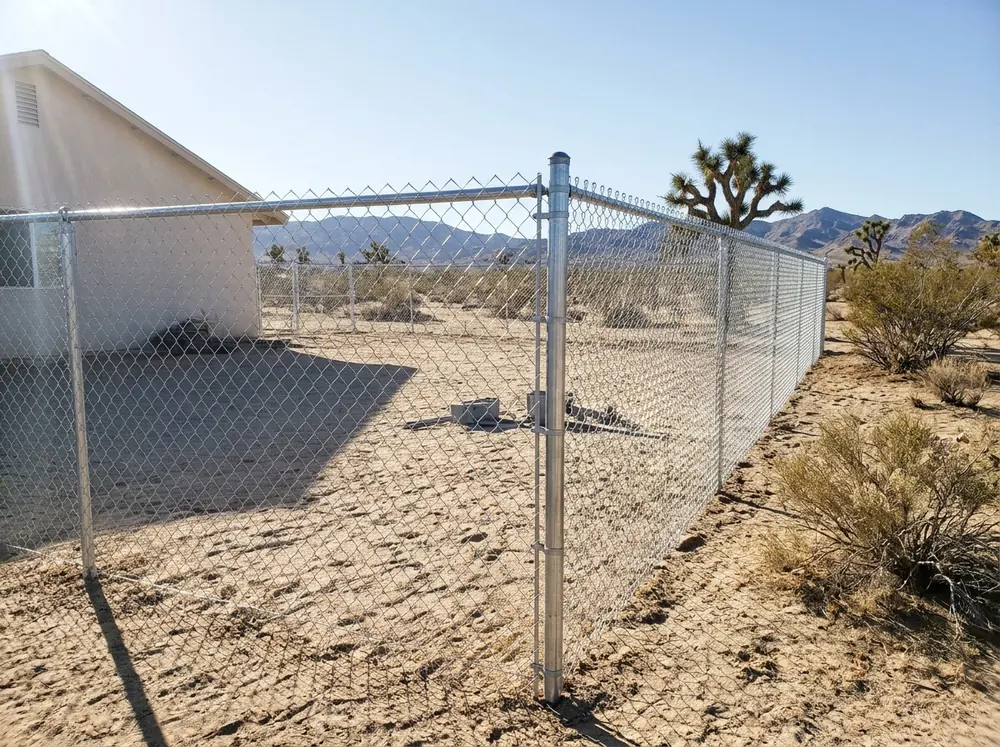 A new galvanized chain link fence with a top rail around a sandy back yard