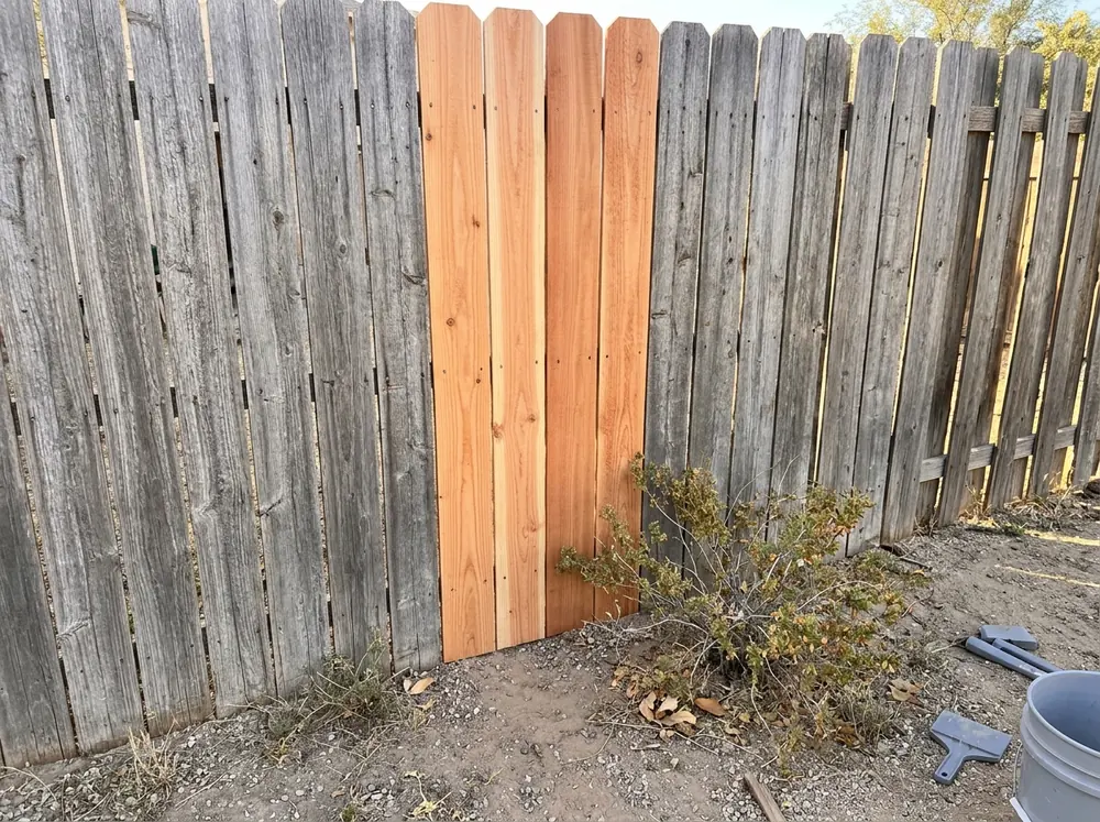 Several new light cedar pickets fitted into a weathered gray wood privacy fence